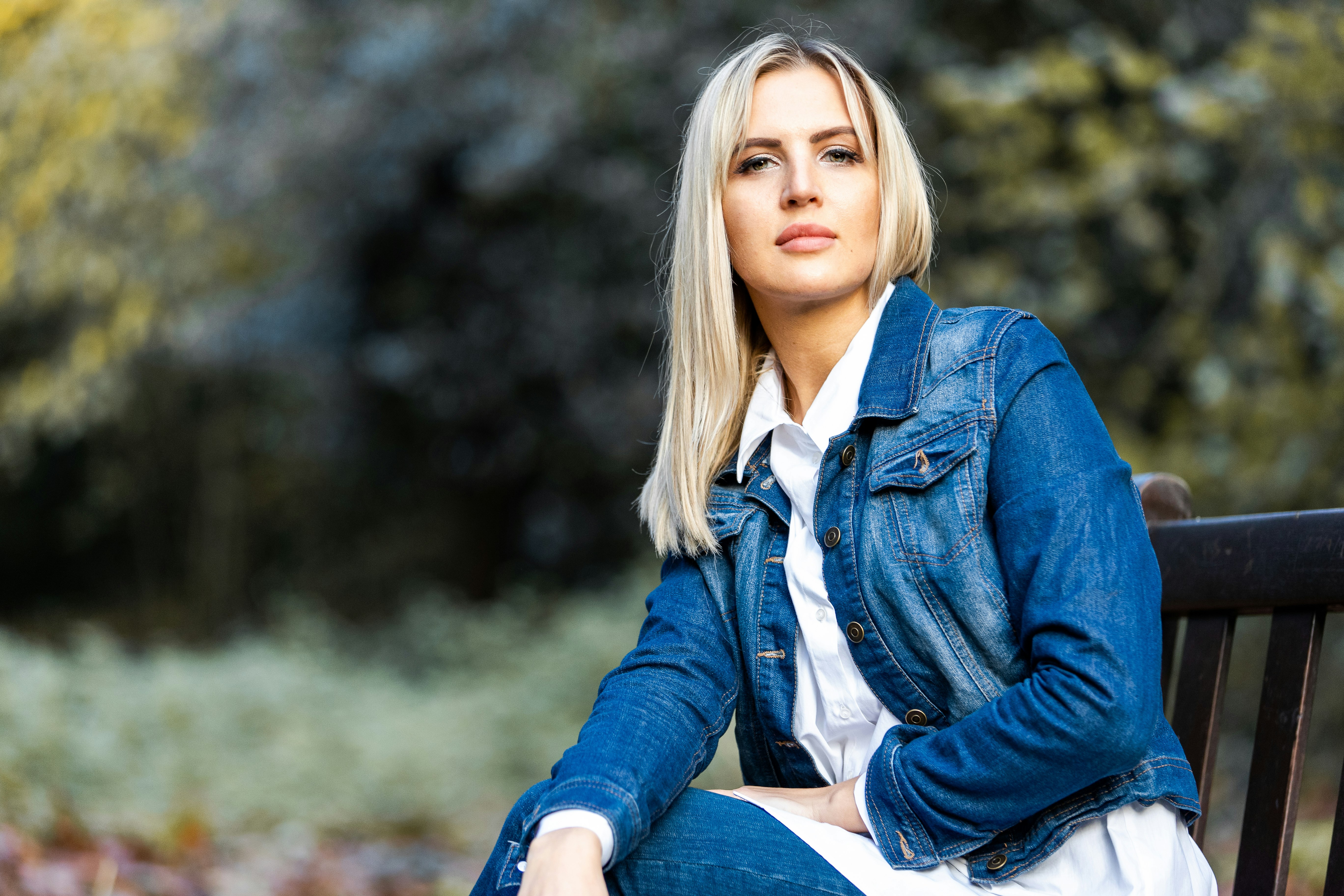 woman in blue denim jacket sitting on brown wooden bench during daytime